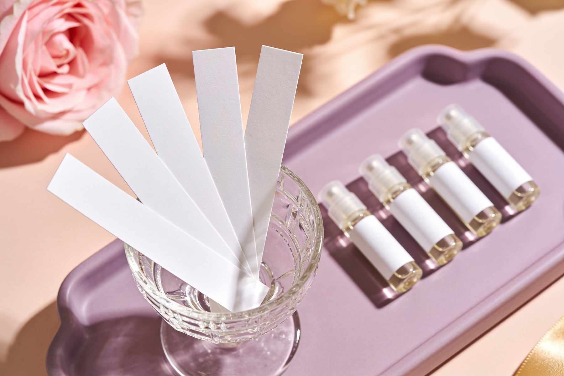 Paper blotter strips fanned in a glass beside small sample vials on a lilac tray.